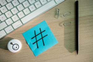 Image of a crowded desktop with a hashtag written a a blue post it note.